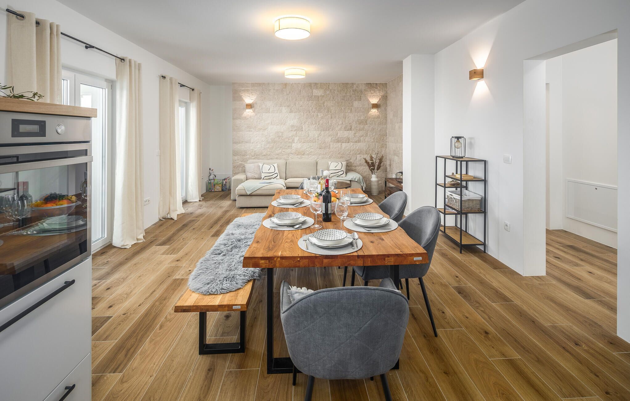 A modern dining room with a wooden table set for six, a grey sofa, and a stone accent wall.
