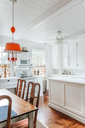 A kitchen with white cabinets, a wooden dining table, and a ceiling fan.