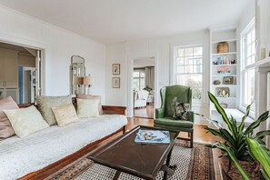 Un salon spacieux comprenant un canapé, un fauteuil et une table basse. On y trouve également une bibliothèque remplie de livres et d’objets décoratifs.