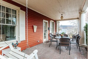 Eine überdachte Veranda mit einer Schaukel, Korbstühlen und einem Tisch.