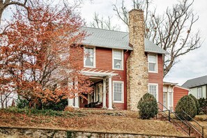 A two-story house with a stone chimney, a porch, and a small staircase leading to the entrance.
