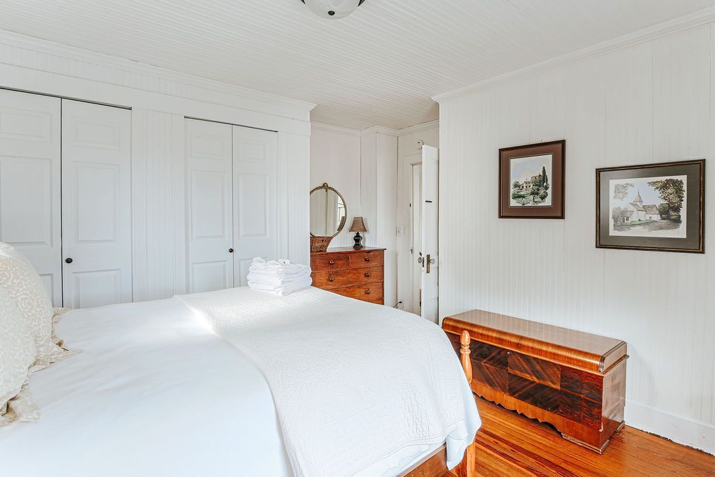Une chambre à coucher avec un grand lit, une commode en bois, un miroir et deux tableaux encadrés accrochés au mur.