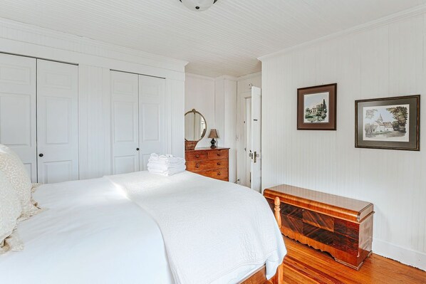 A bedroom with a large bed, a wooden dresser, a mirror, and two framed pictures on the wall.