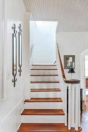 Un escalier aux murs blancs et aux marches en bois menant à un palier.