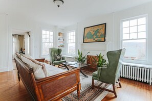 A spacious living room with a wooden sofa, green armchairs, a coffee table, and a large world map on the wall. - The Cardinal House: Historic Home on Tree Streets (Waynesboro)