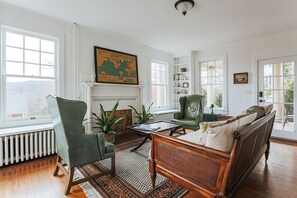 A spacious living room with a fireplace, a green armchair, a wooden sofa, and a large world map on the wall.