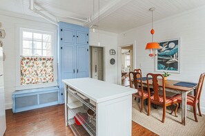 Une cuisine avec un îlot central blanc, des armoires bleues et un coin repas comprenant des chaises et une table en bois.