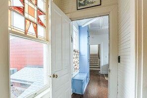 A narrow hallway with a blue bench, a door leading to a room with a red exterior, and a staircase in the background. - The Cardinal House: Historic Home on Tree Streets (Waynesboro)