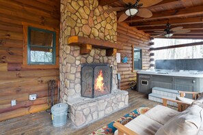 A log cabin interior with a stone fireplace, wooden walls, a ceiling fan, and a hot tub.