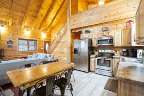 A cabin interior with a wooden interior, a dining area, a kitchen with modern appliances, and a staircase.