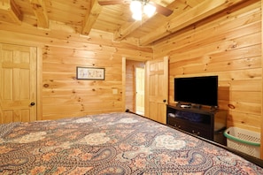Una habitación con paneles de madera, una cama, un televisor y una puerta que da a otra habitación.