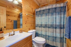 A wooden cabin bathroom with a white sink, a mirror, a toilet, and a shower curtain.