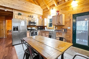 A wooden cabin kitchen with a stainless steel refrigerator, a microwave, a stove, and wooden cabinets.
