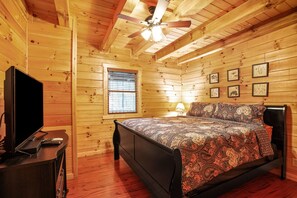 A wooden cabin bedroom with a bed, a ceiling fan, a TV, and framed pictures on the wall.
