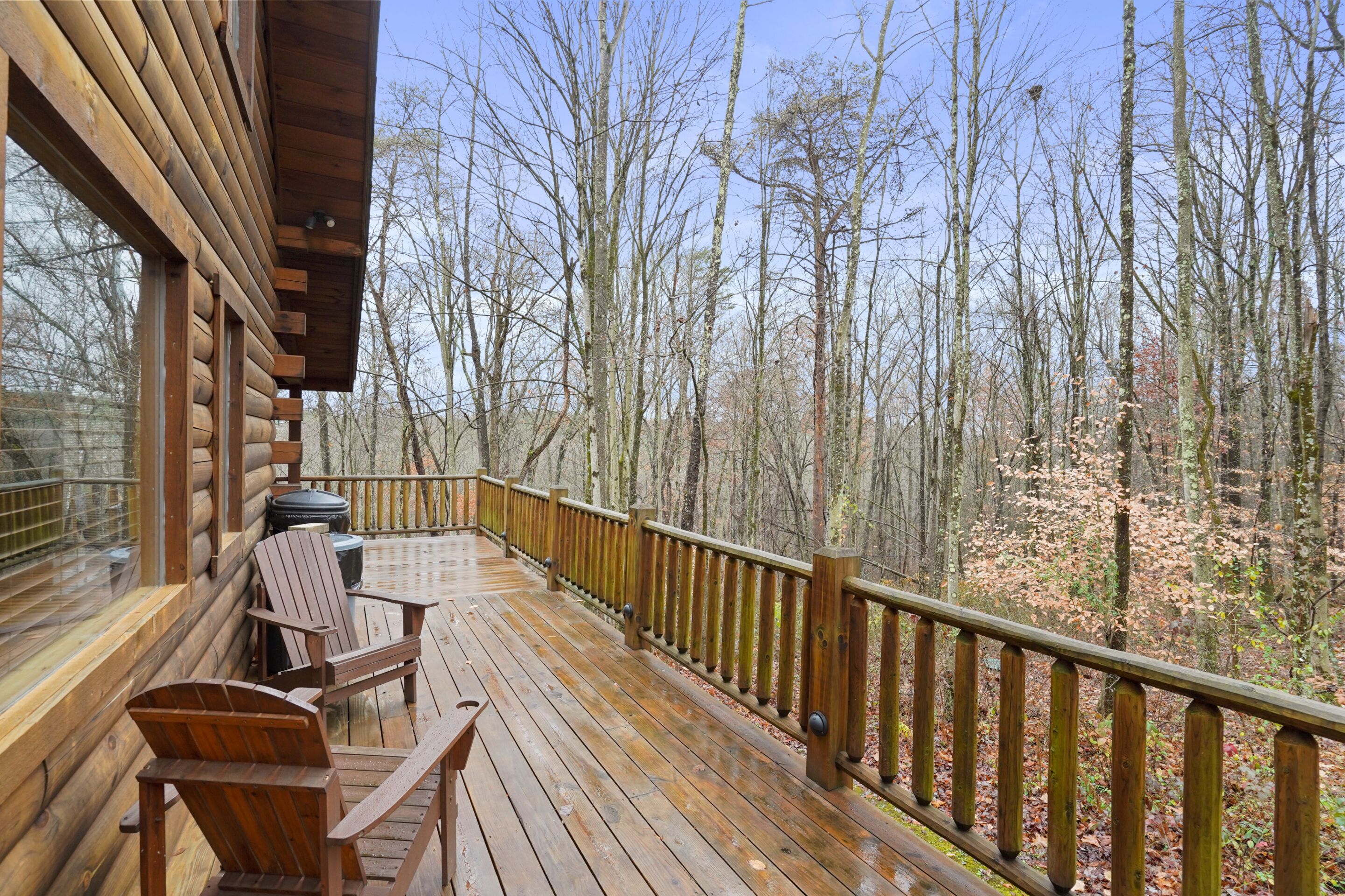Una terraza de madera con vistas a un bosque, una parrilla y un banco.