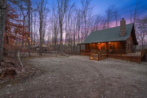 A rustic cabin with a stone chimney, wooden deck, and a gravel driveway.