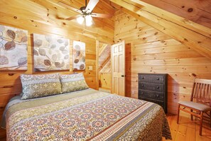 Ein Schlafzimmer einer Holzhütte mit einem Bett, einer Kommode, einem Sessel und einem Deckenventilator.
