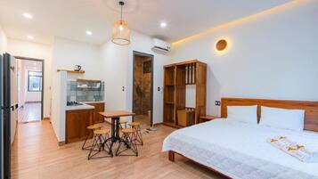 Quarto com cama, guarda-roupa de madeira, kitchenette e área de refeições com bancos.