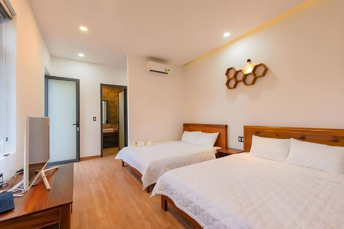 Habitación de hotel con dos camas, un escritorio con computadora, un equipo de aire acondicionado y una lámpara de pared.