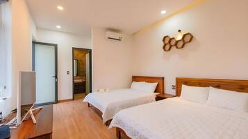 Quarto de hotel com duas camas, uma escrivaninha com computador, aparelho de ar condicionado e luminária fixada na parede.