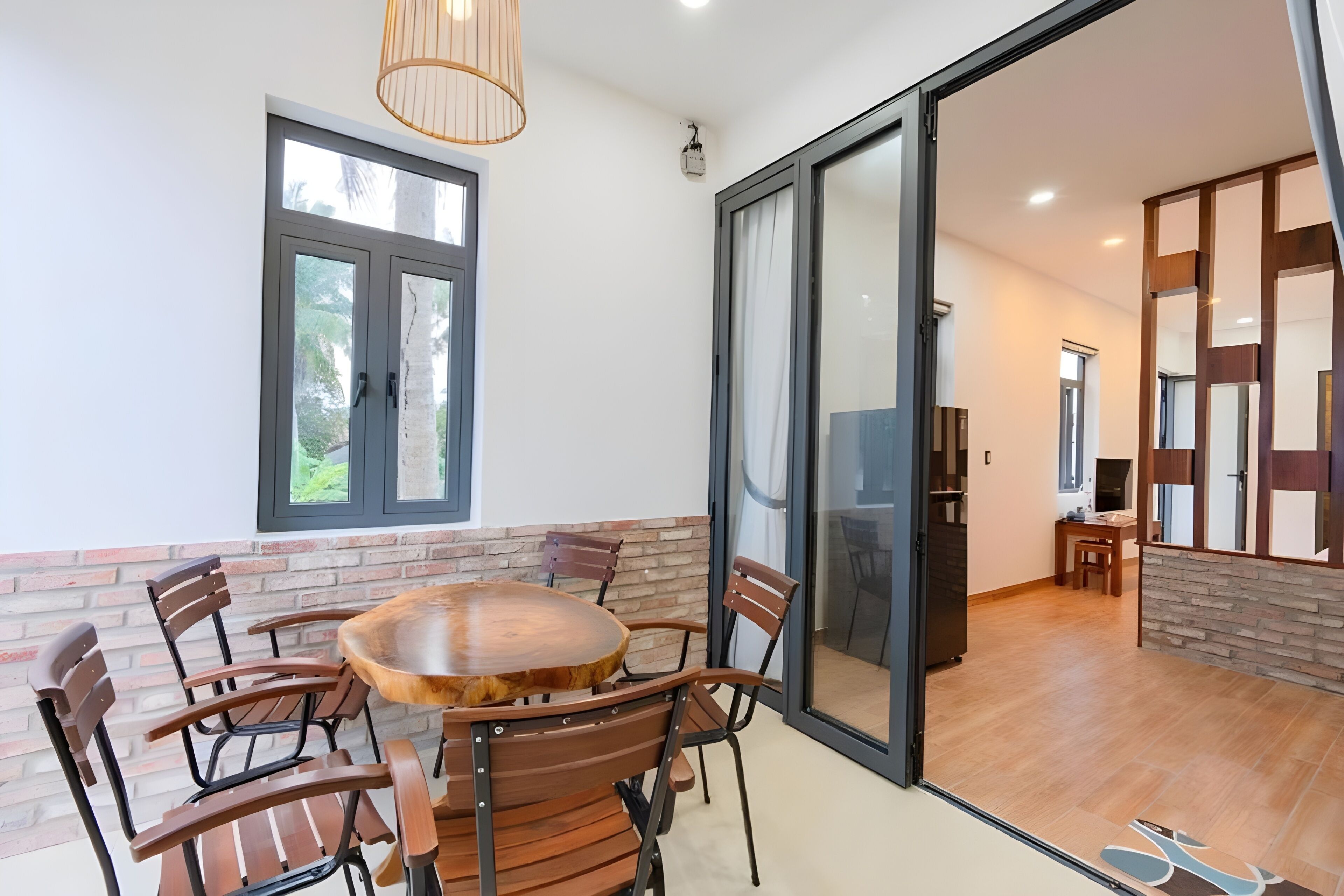 A dining area with a round wooden table and chairs, a window with a view, and a sliding glass door leading to another room.