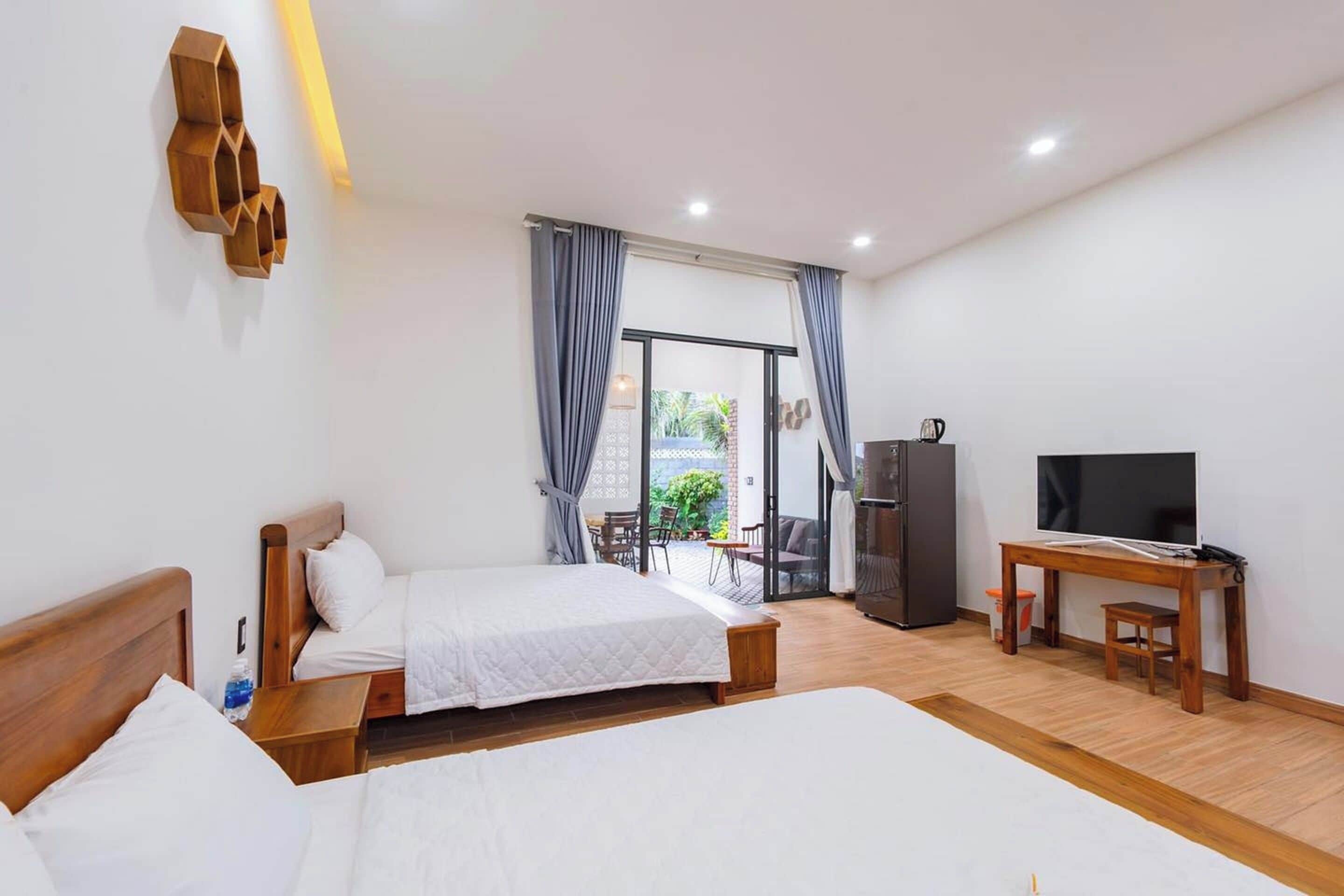 A hotel room with two beds, a TV, a desk, and a view of the outdoors.