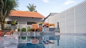 A swimming pool with a clear view of the surrounding area, including a house with a tiled roof and a white wall with a perforated pattern. - Nhu House Apartment Phu Quoc  (Phu Quoc)