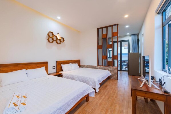 Une chambre d’hôtel avec deux lits, un bureau en bois, une télévision et une grande fenêtre.