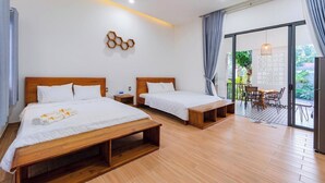 A hotel room with two beds, a wooden floor, a balcony with a table and chairs, and a view of greenery outside. - Nhu House Apartment Phu Quoc  (Phu Quoc)