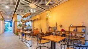 A cozy cafe with wooden tables and chairs, shelves with books and plants, and a patterned floor. - Nhu House Apartment Phu Quoc  (Phu Quoc)