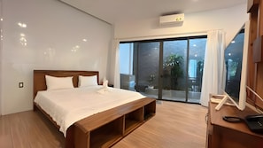 Une chambre moderne avec un lit en bois, un banc intégré, une grande porte-fenêtre coulissante donnant sur un balcon et un appareil de climatisation fixé au plafond.