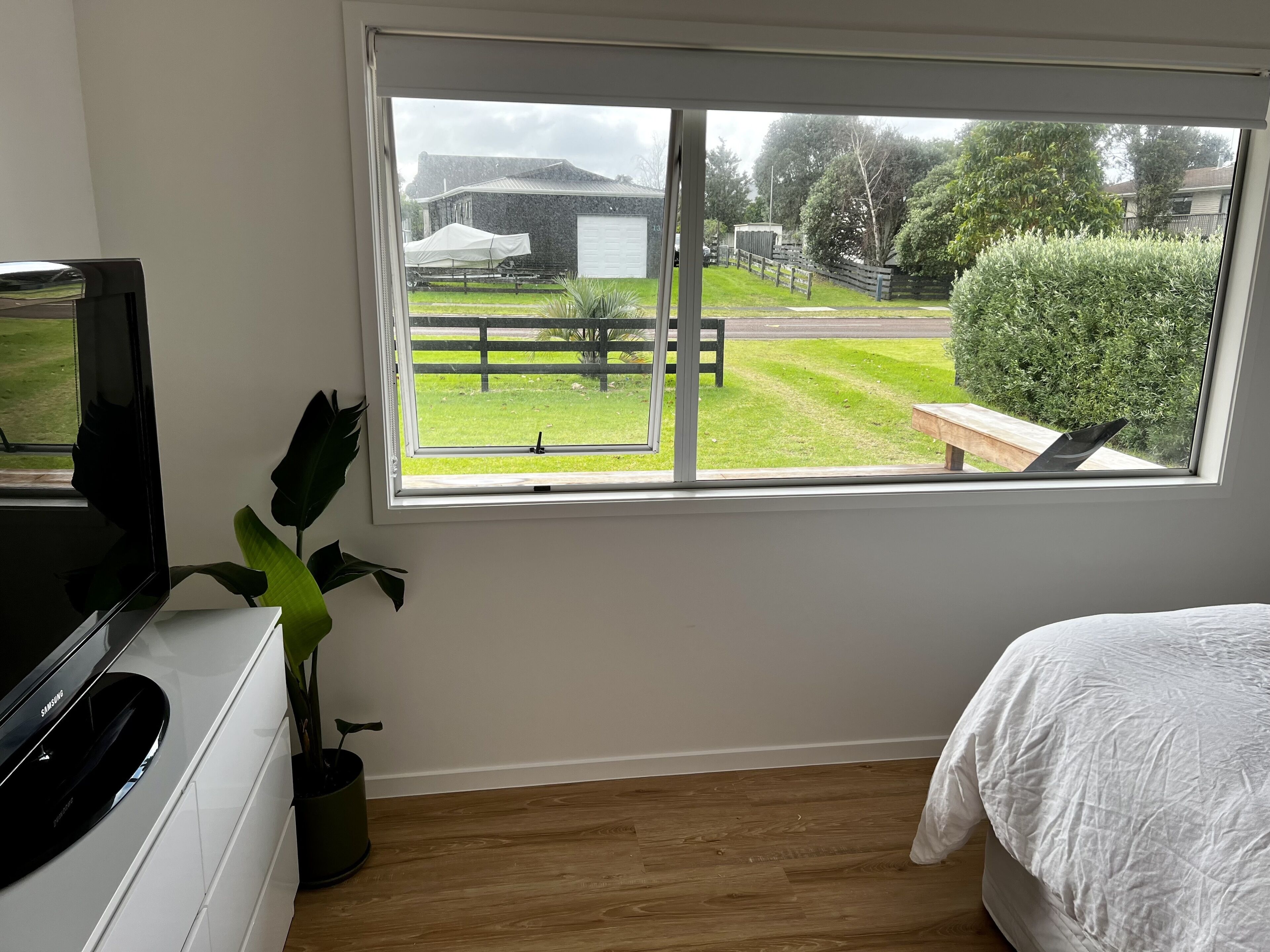 A bedroom with a large window, a bed, a TV, and a plant.