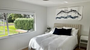 Ein Schlafzimmer mit einem großen Bett, einem Fenster, einem Nachttisch und einem Wandbild.
