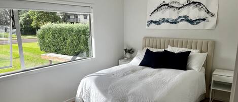 Een slaapkamer met een groot bed, een raam, een nachtkastje en een kunstwerk aan de muur.
