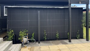 Ein moderner Außenbereich mit einem schwarzen Metallzaun, einer Holzbank und einem Gartenschlauch.