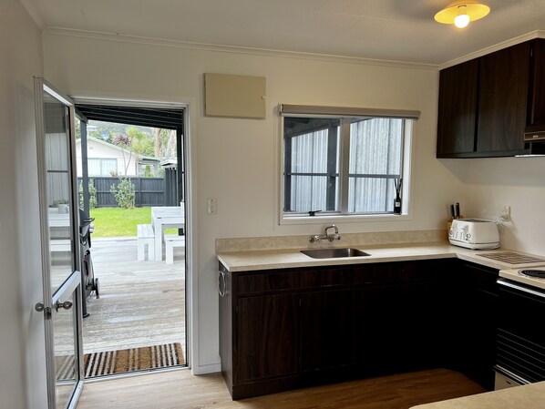 A compact kitchen with dark wooden cabinets, a white countertop, a built-in sink, and a window above the sink.