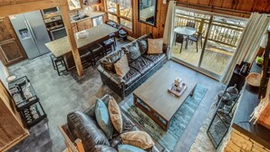 A spacious living area with a leather sofa, a coffee table, and a dining table. There is a kitchen area with a refrigerator, oven, and sink. The space has large windows and a view of the outdoors.