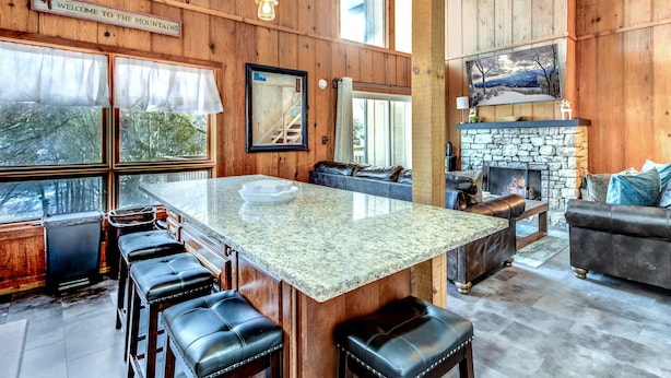A wooden interior with a stone fireplace, a large island with bar stools, and a couch.