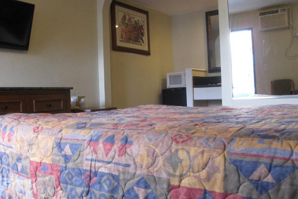 A bedroom with a bed, a dresser, a television, a microwave, and a large mirror.