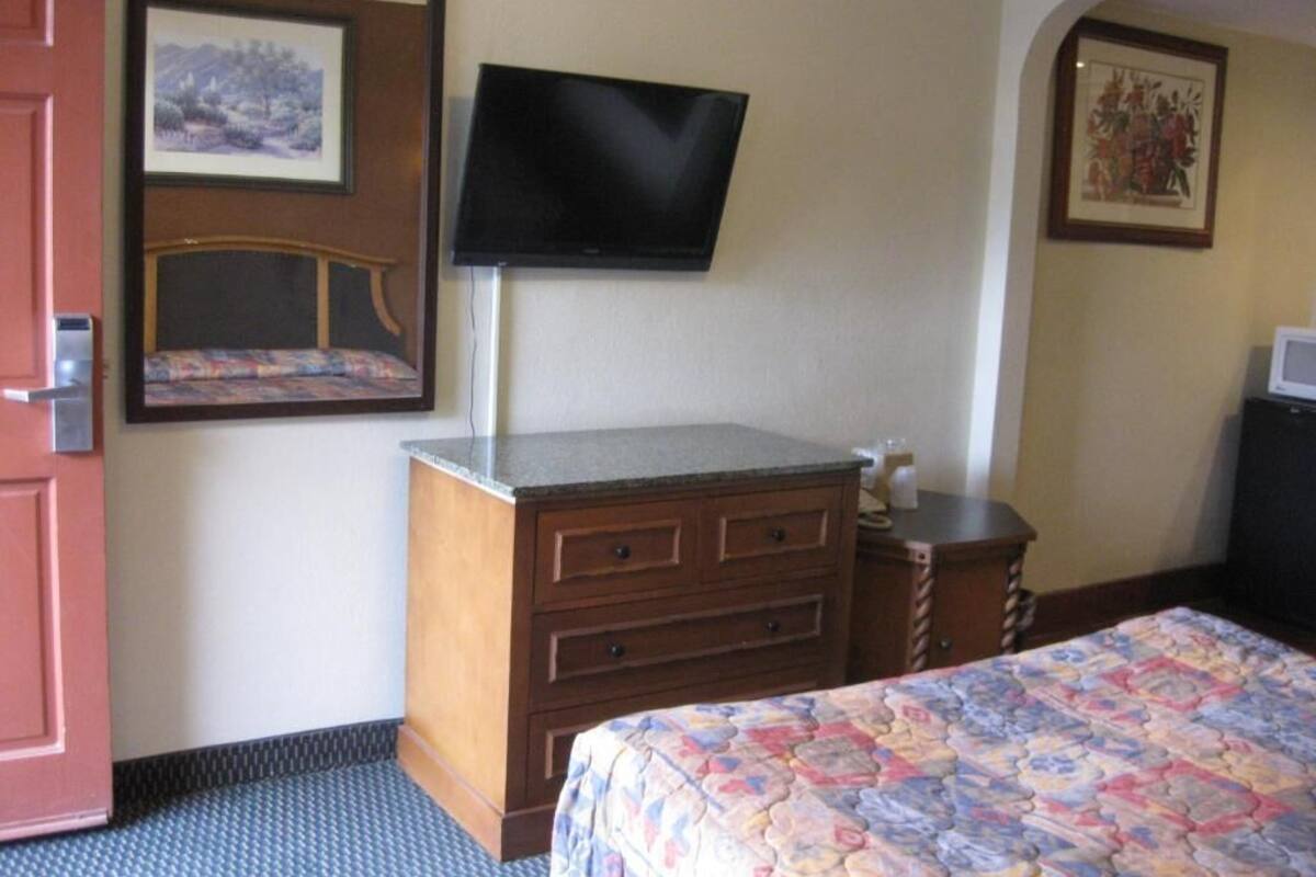 A hotel room with a bed, a dresser, a television mounted on the wall, and two framed pictures on the walls.
