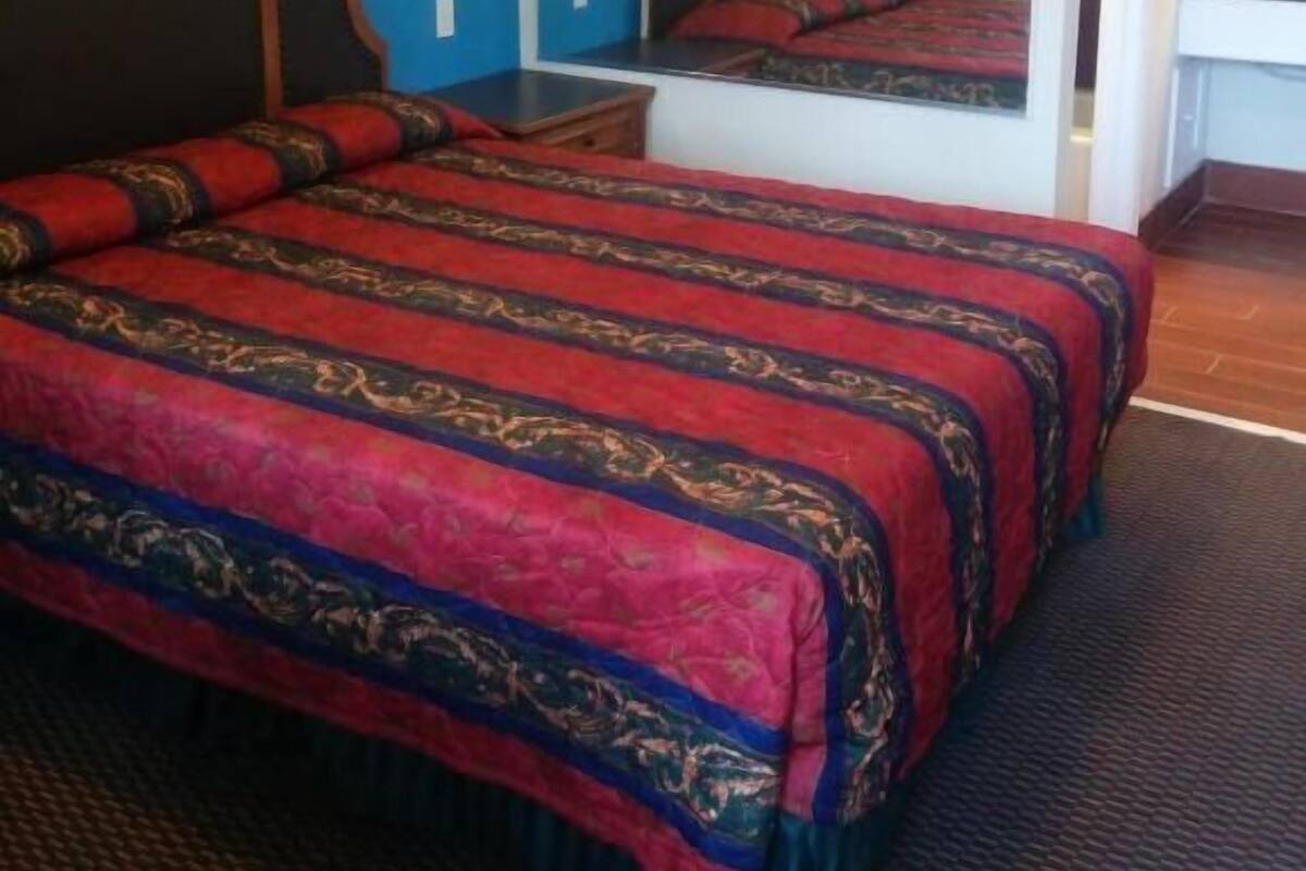 A hotel room with a large bed, a desk, and a mirror.