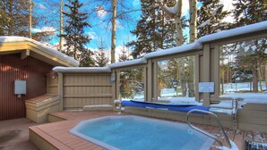 A hot tub surrounded by a wooden deck, with a covered area and a sign indicating it is for ski hill guests.