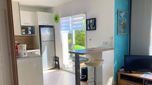 A modern kitchen with a refrigerator, microwave, and coffee maker. There is a dining area with a bar stool and a TV stand. - Casa Azul Turquesa (Lumio)