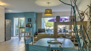 A modern living room with a dining area, a television, and a view of the outdoors. - Casa Azul Turquesa (Lumio)