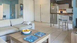 A modern living room with a sofa, a coffee table with a bowl of fruit, and a kitchen area with a refrigerator and microwave. - Casa Azul Turquesa (Lumio)