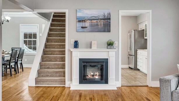 Un intérieur moderne comprenant un escalier, une cheminée, un coin repas, une cuisine et un tableau au mur.
