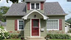 Une maison à deux étages avec une porte d’entrée rouge, des volets blancs et un petit porche.