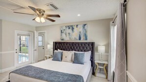 A bedroom with a large bed, a ceiling fan, a painting on the wall, and a view of the outside. - Disney & Universal Studios Vacation Home (Kissimmee)