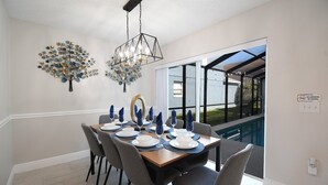A dining area with a table set for four, a chandelier, and wall art. - Disney & Universal Studios Vacation Home (Kissimmee)