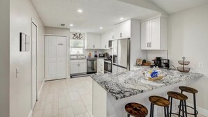 A modern kitchen with white cabinets, a granite countertop, and a built-in island with stools. - Disney & Universal Studios Vacation Home (Kissimmee)